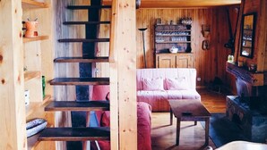 A wooden interior with a staircase, a sofa, a table, and shelves with various items. - Large chalet La Clusaz - Exceptional view of the Aravis mountains in the Balme sector (La Clusaz)