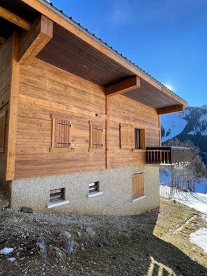 Een houten chalet met balkon, gelegen tegen een bergachtige achtergrond.