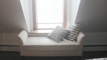 A corner seating area with a cushioned bench, a window with blinds, and two pillows.