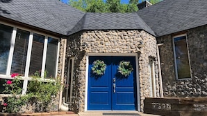 Un bâtiment en pierre avec une porte bleue, deux couronnes de fleurs et un mur en pierre.