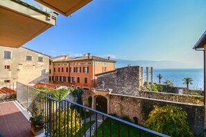 A balcony with a view of the sea, a stone wall, and a building with a tiled roof. - LAWRENCE'S FORMER MANSION WITH BALCONY AND LAKE VIEW (Gargnano)