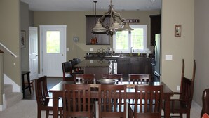 A spacious kitchen with a central island, wooden chairs, and a hanging light fixture.