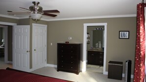 A bedroom with a bed, a dresser, a ceiling fan, a door, and a mirror.