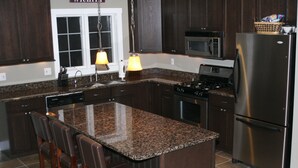 A kitchen with granite countertops, dark wooden cabinets, stainless steel appliances, and a bar stool seating area.