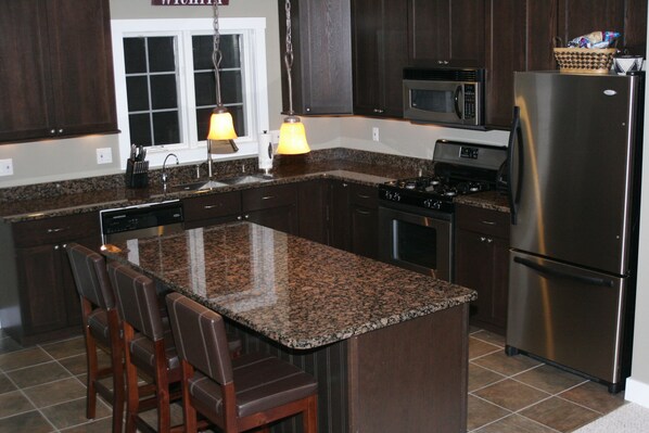 A kitchen with granite countertops, dark wooden cabinets, stainless steel appliances, and a bar stool seating area. - Sugarbush Resort; Spectacular Town Home! Discounts available at the Après Chalet (Warren)