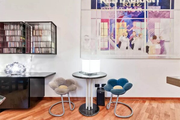 A modern room with a black bookshelf, a round table with a lamp, and two chairs with a unique design.