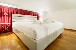 A modern bedroom with a large bed, red curtains, and a wooden floor.