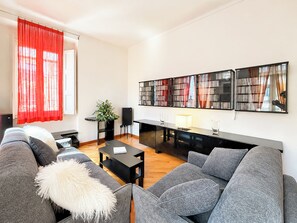 A modern living room with a grey sofa, a small table, and a bookshelf.