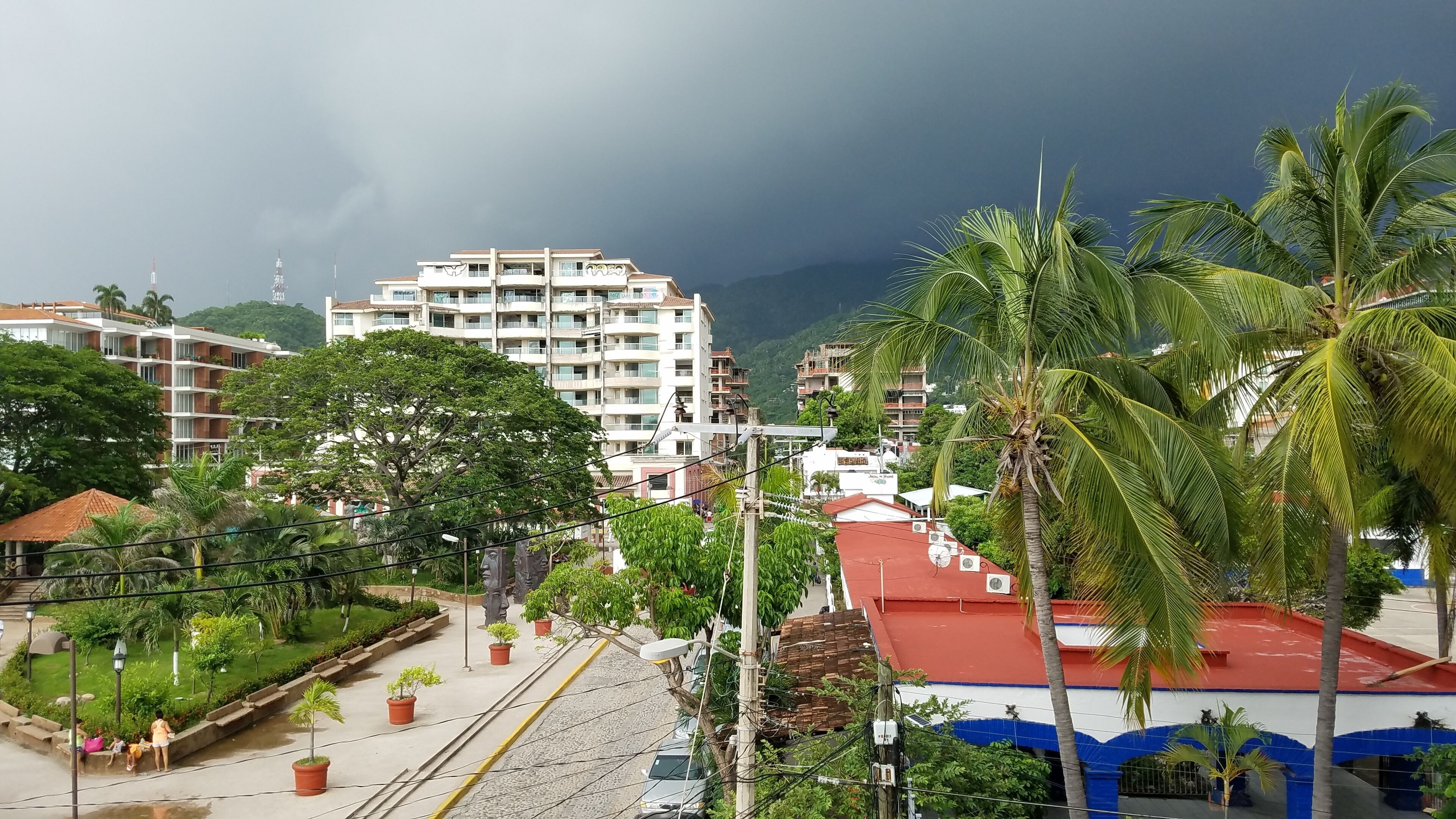 A multi-story building with balconies, surrounded by lush greenery and palm trees.