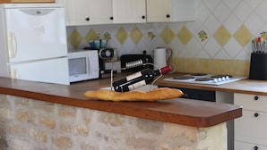A kitchen with a stone countertop, a white refrigerator, a microwave, a toaster, and a wine bottle on a baguette. - Spacious 3 Bed Gite, Aude, Pool, Hot Tub, Free Wi-fi, Games Room, Pet-Friendly! (Arques)