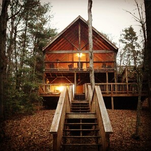 Een houten chalet met twee verdiepingen, voorzien van een balkon op de bovenste etage, omringd door bomen.