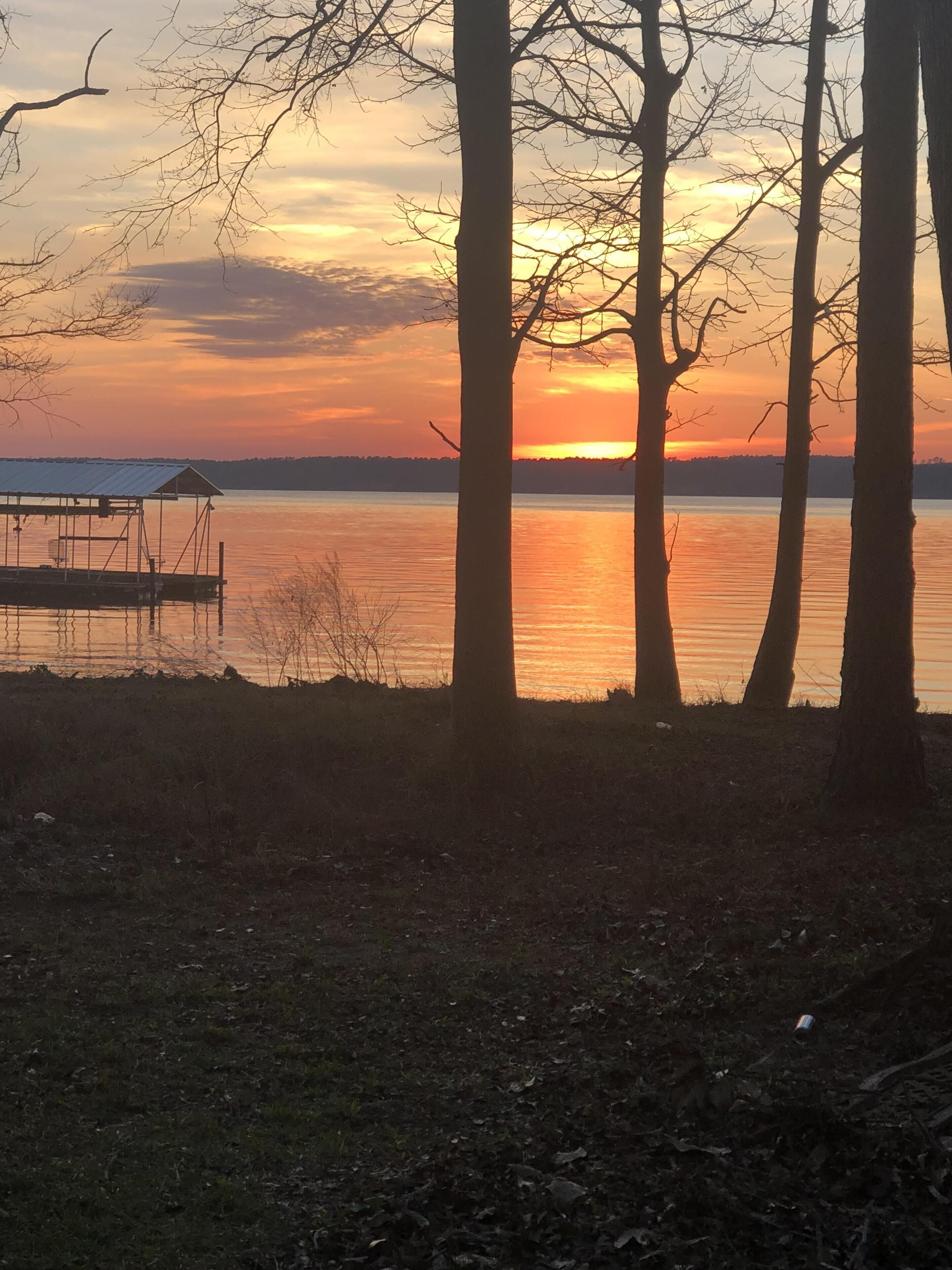 Un coucher de soleil sur un lac paisible, avec des arbres sans feuilles et un quai.