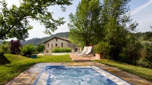 Un jacuzzi dans un jardin, avec une maison en pierre en arrière-plan.