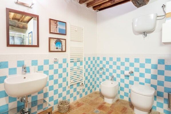 A bathroom with a checkered tile wall, a sink, a bidet, and a toilet.
