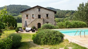 Un bâtiment en pierre doté d’une piscine, entouré de verdure et de collines.
