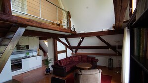 A spacious loft with exposed wooden beams, a kitchen with white cabinets, a red sofa, and a small round table. - NEW !  Spacious apartment on 2 floors for 2-3 people (Baiersbronn)