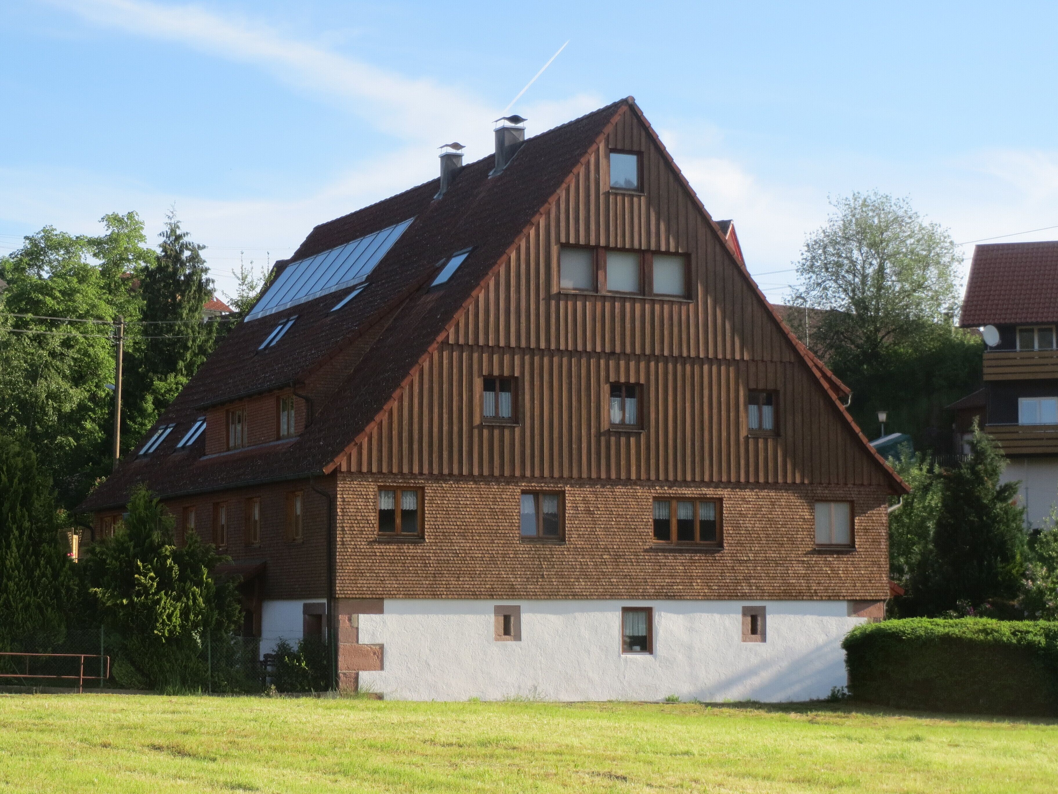 A two-story house with a sloped roof, multiple windows, and a solar panel on the roof.