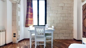 Ein Zimmer mit Stehwand, einem Fenster mit Vorhang, einem weißen Tisch und einem Stuhl sowie einem Heizkörper.