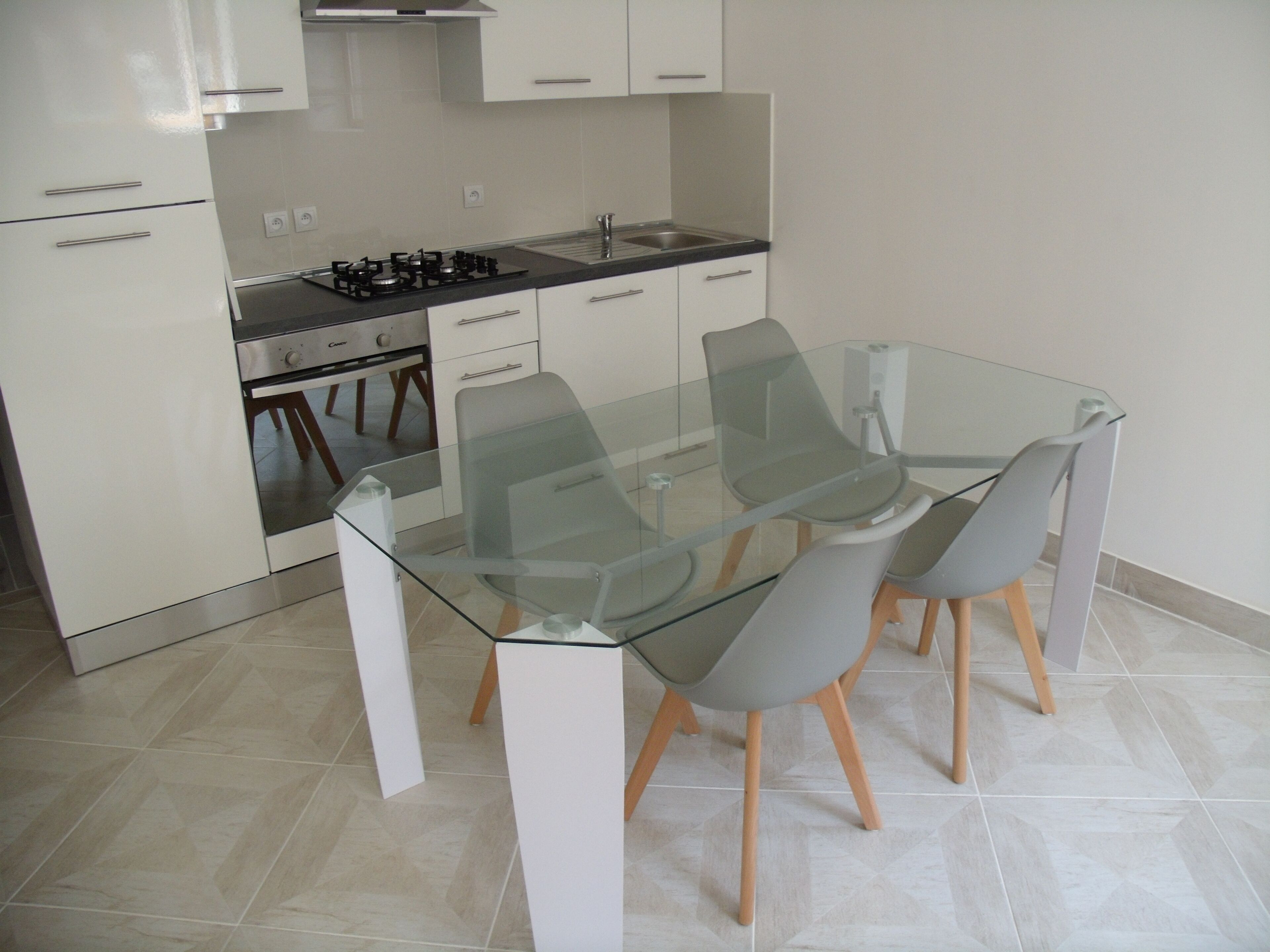 A modern kitchen with white cabinets, a gas stove, and a glass dining table with chairs.