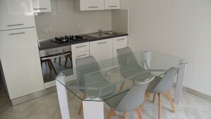 A modern kitchen with white cabinets, a gas stove, and a glass dining table with chairs. - Promo Aptn2 T3 and garden 50 meters from the beach  (Hendaye)