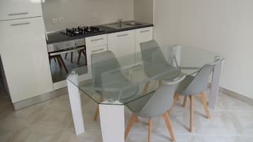 A modern kitchen with white cabinets, a gas stove, and a glass dining table with chairs.