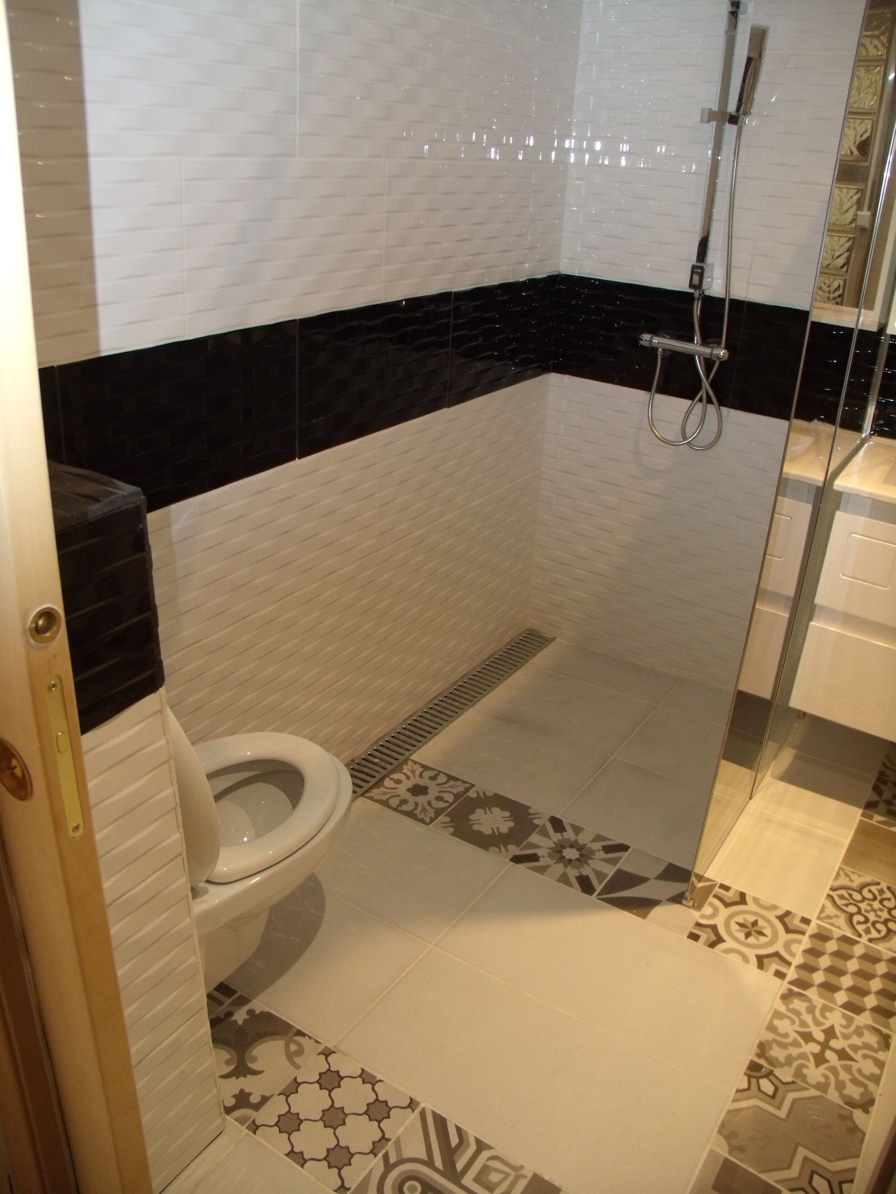 Un baño con inodoro, ducha y baldosas estampadas.