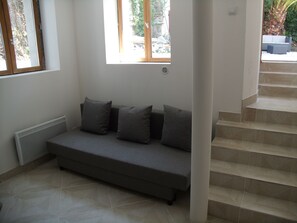 Un salon moderne avec un canapé gris, un radiateur, une fenêtre et un escalier.