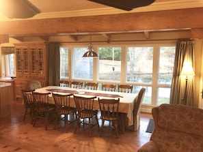 Een eetruimte met een houten tafel en stoelen, grote ramen en uitzicht op een meer.