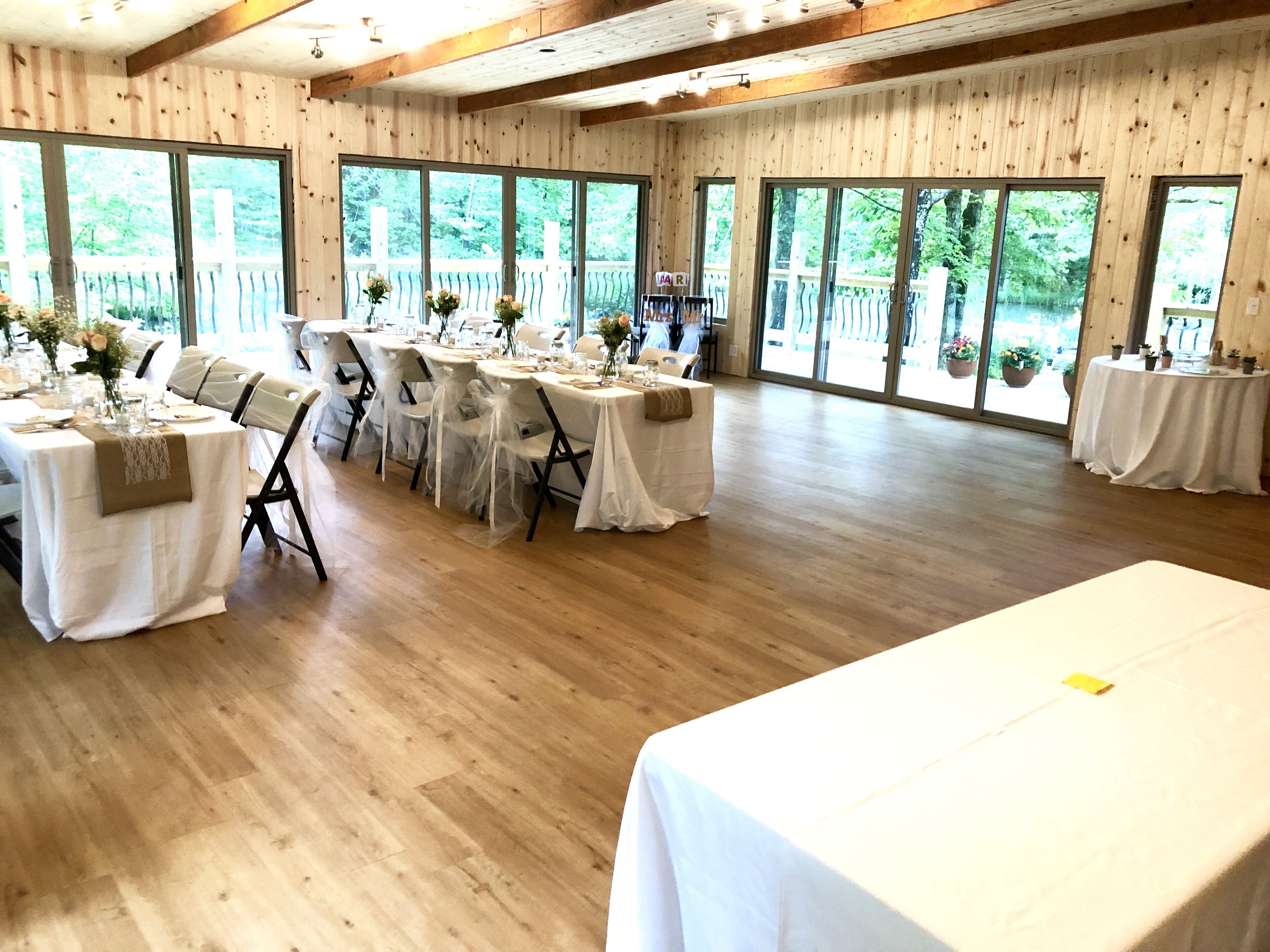 A large room with multiple tables set for dining, large windows, and wooden floors.