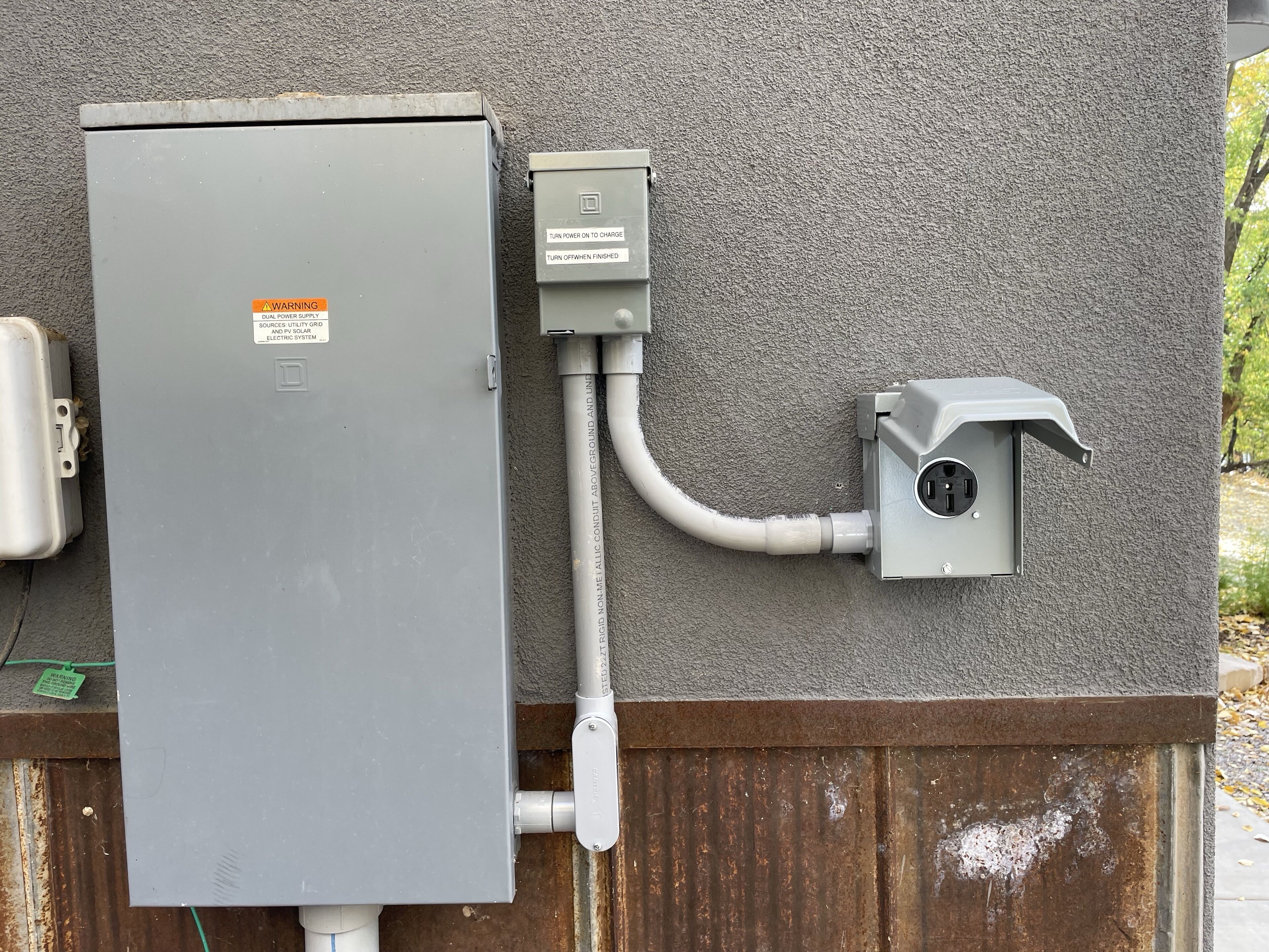 Un boîtier de compteur d’électricité fixé sur un mur texturé, avec un conduit métallique qui y est raccordé.