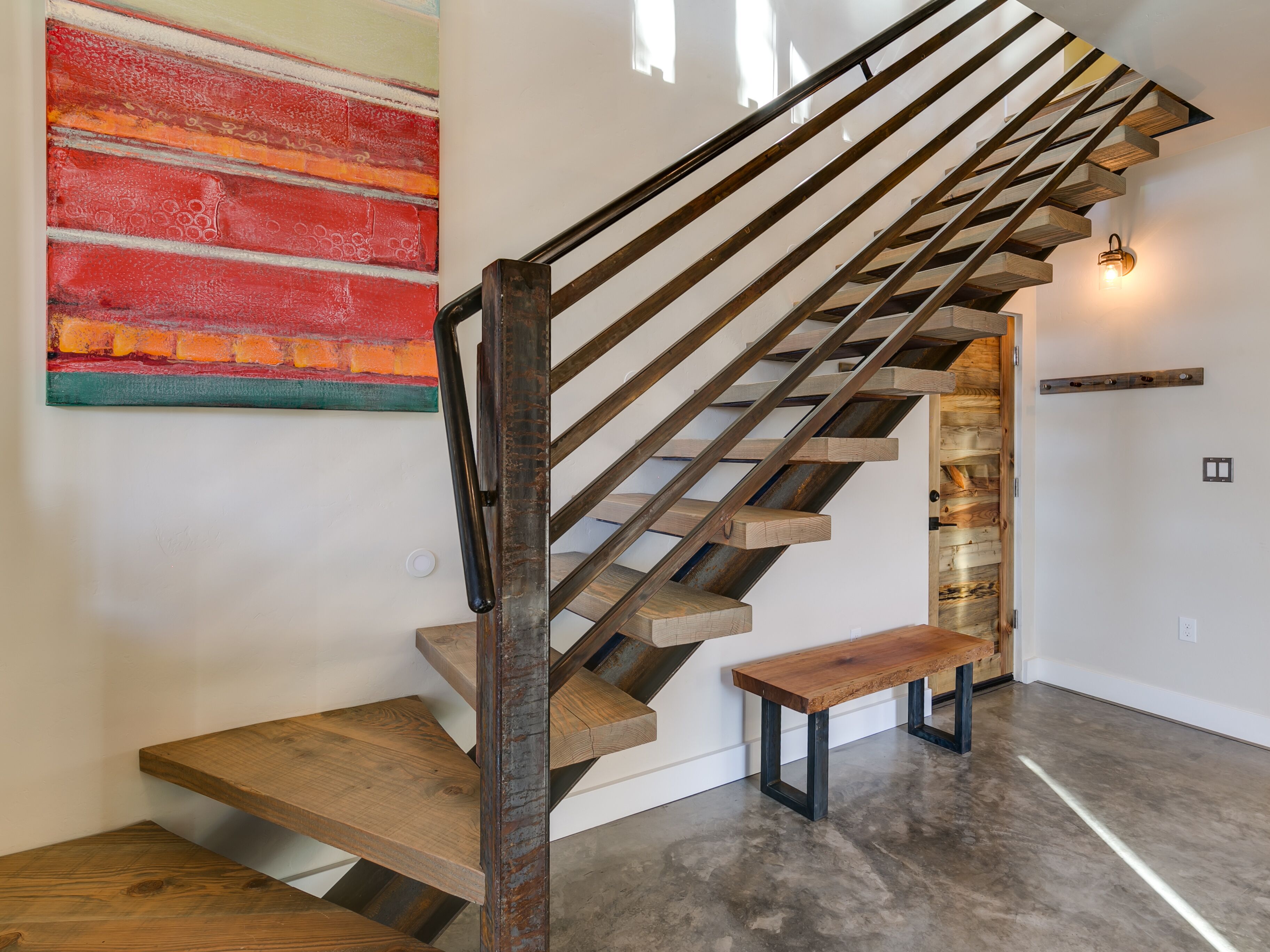 Eine Holztreppe mit einer Bank, einer Lampe und einem farbenfrohen, abstrakten Gemälde an der Wand.