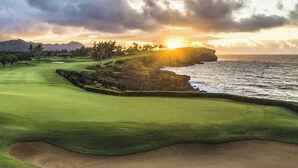 Un campo de golf con vista al océano y a las montañas al atardecer.