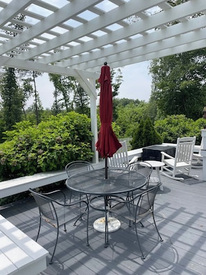 Una terrazza esterna con un tavolo e sedie rotonde in metallo, un ombrello rosso e sedie in legno bianco.