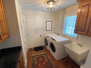 A laundry room with a washing machine, dryer, sink, and a door. - Moss Side Cottage | Peaceful Meadow Retreat (New Kent)