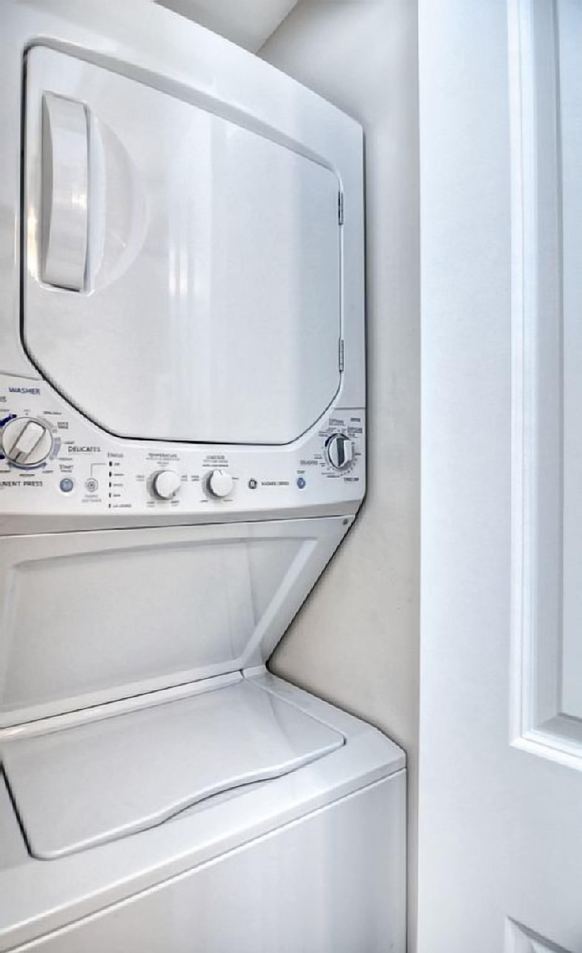 A front view of a white washing machine and dryer stacked in a corner.