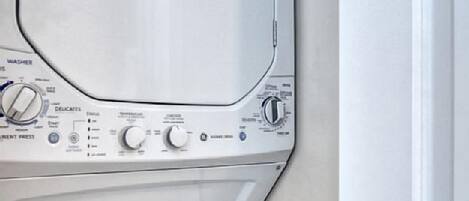 A front view of a white washing machine and dryer stacked in a corner.