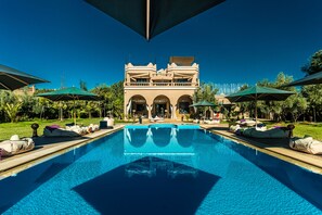 A swimming pool with lounge chairs and umbrellas, a building with arched entrances, and a clear blue sky. - The Bird Exclusive Guest House & Spa (Marrakech)