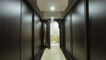 A narrow, dark wooden hallway with a tiled floor leading to a bathroom with a white sink and a towel rack.