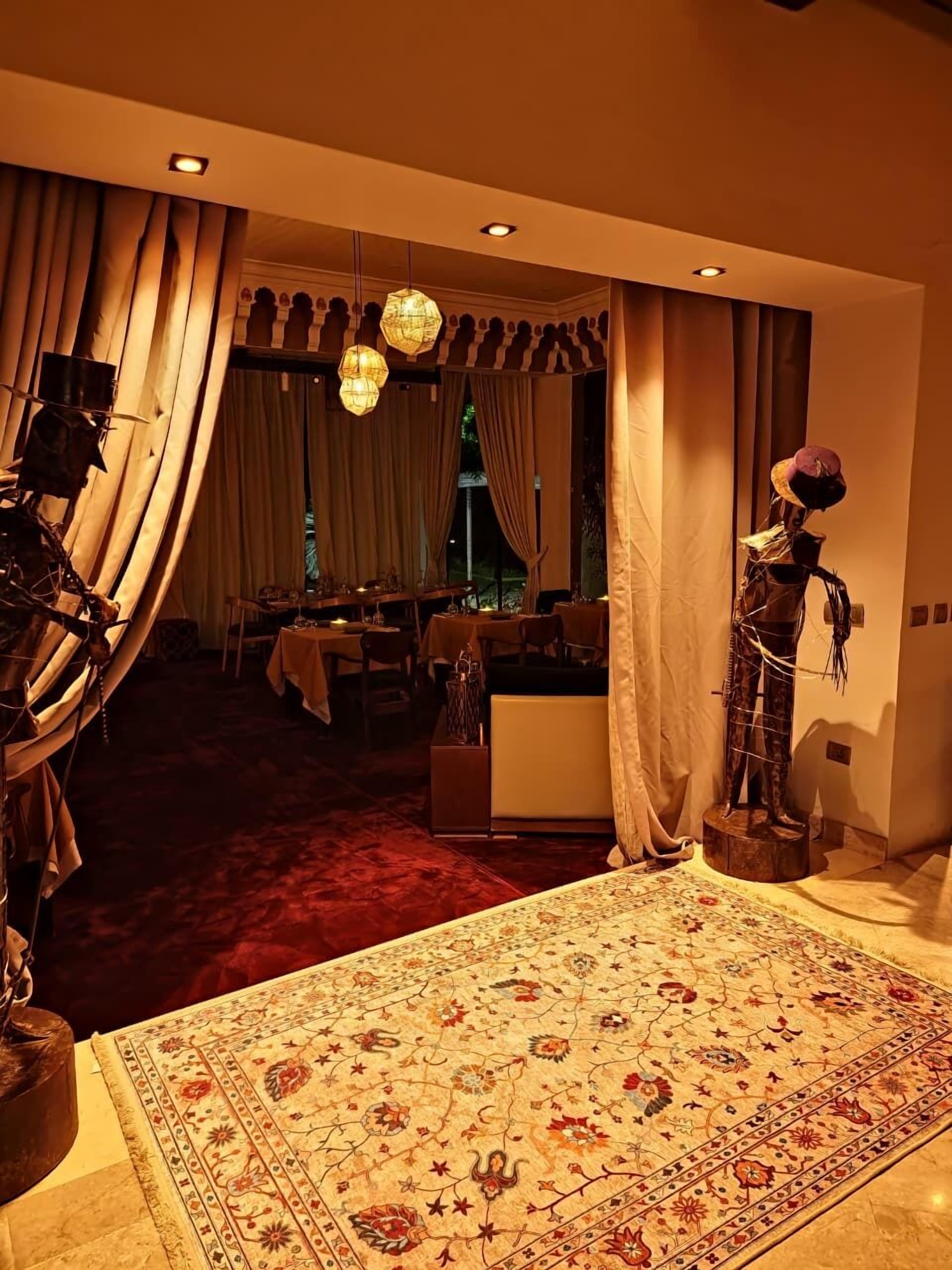 A room with a patterned carpet, a dining area with a table set for two, and a decorative sculpture.