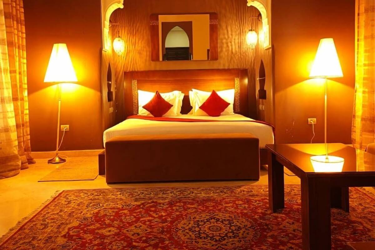 A hotel room with a large bed, two bedside lamps, a small table, and a patterned rug.