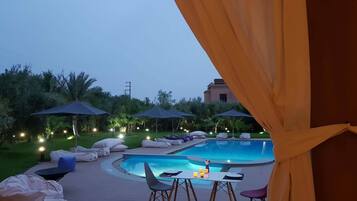 Zona de piscina con sillones reclinables, sombrillas y una mesa con sillas.