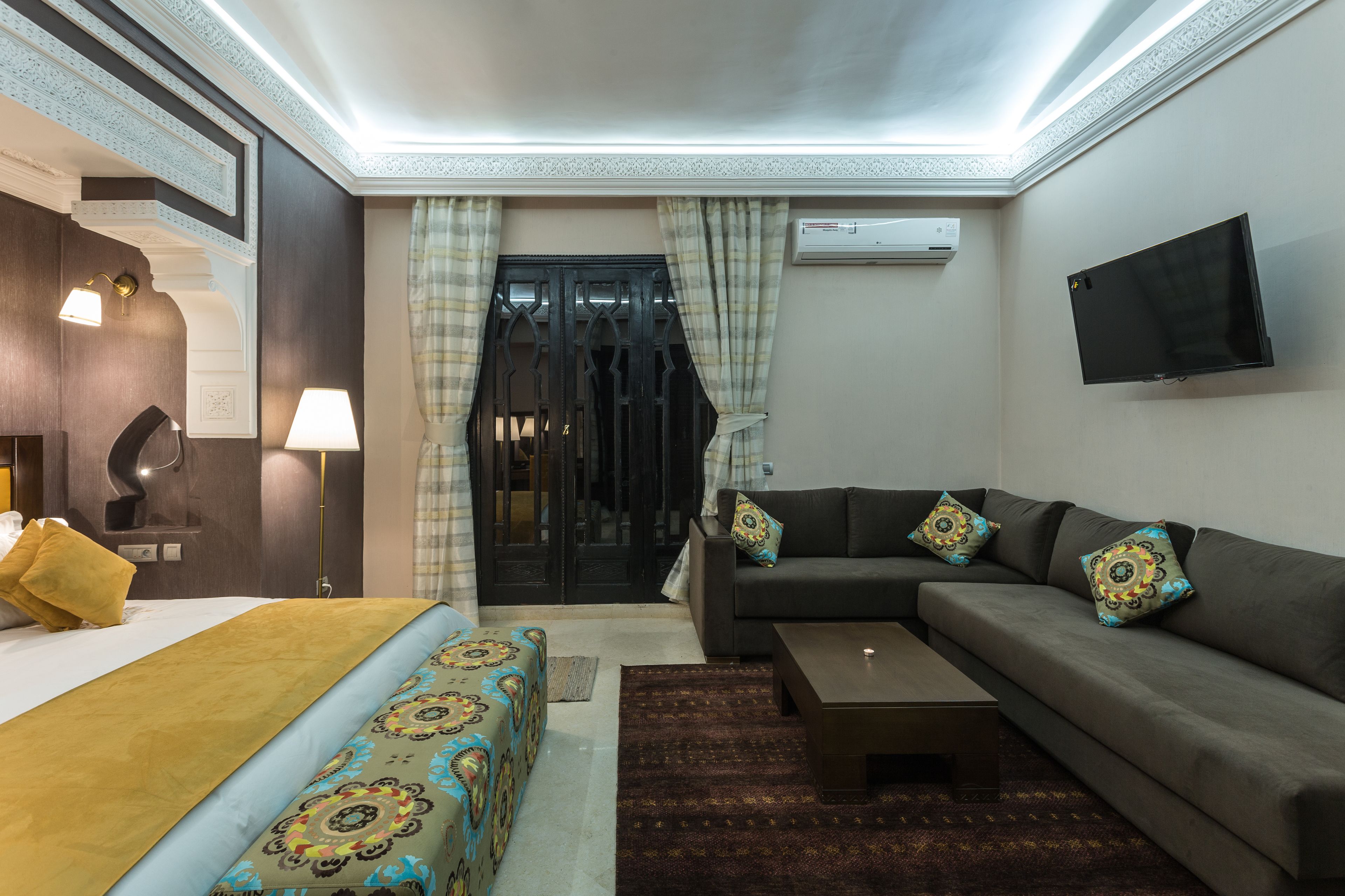 A hotel room with a bed, a sofa, a coffee table, and a TV mounted on the wall.