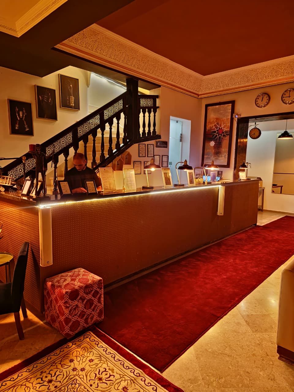 A hotel lobby with a reception desk, a staircase, and a red carpet.