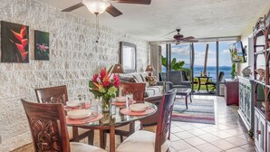 A dining area with a glass table and chairs, a ceiling fan, and a view of the ocean.