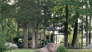 A park with a playground, including a slide and climbing structures, surrounded by trees and rocks. - Cute and spacious single family home, pet friendly (Charlotte)