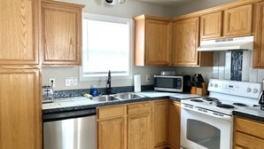 A kitchen with wooden cabinets, a stainless steel dishwasher, a microwave, a stove, and a window providing natural light. - Cute and spacious single family home, pet friendly (Charlotte)