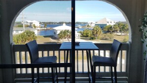 Un balcon avec deux fauteuils en osier et une petite table, donnant sur une marina où l’on peut admirer des bateaux et des maisons.