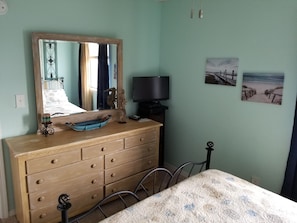 A bedroom with a wooden dresser, a bed with a quilt, a large mirror, a television, and two wall-mounted pictures.