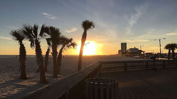 A wooden boardwalk with palm trees and a sunset in the background.