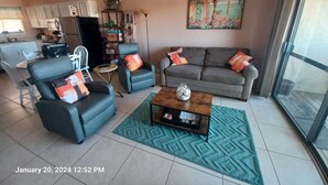 Un salon avec un canapé, des fauteuils, une table basse et un tableau accroché au mur.
